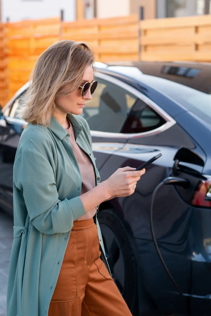 Woman using her phone beside an electric car while it charges.