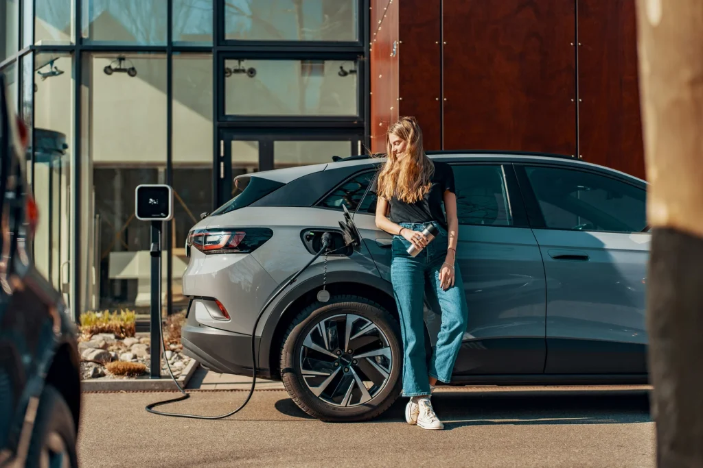 Woman standing beside an electric car at a charging point.