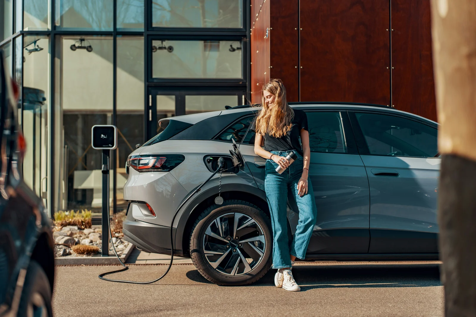 Woman standing beside an electric car at a charging point.