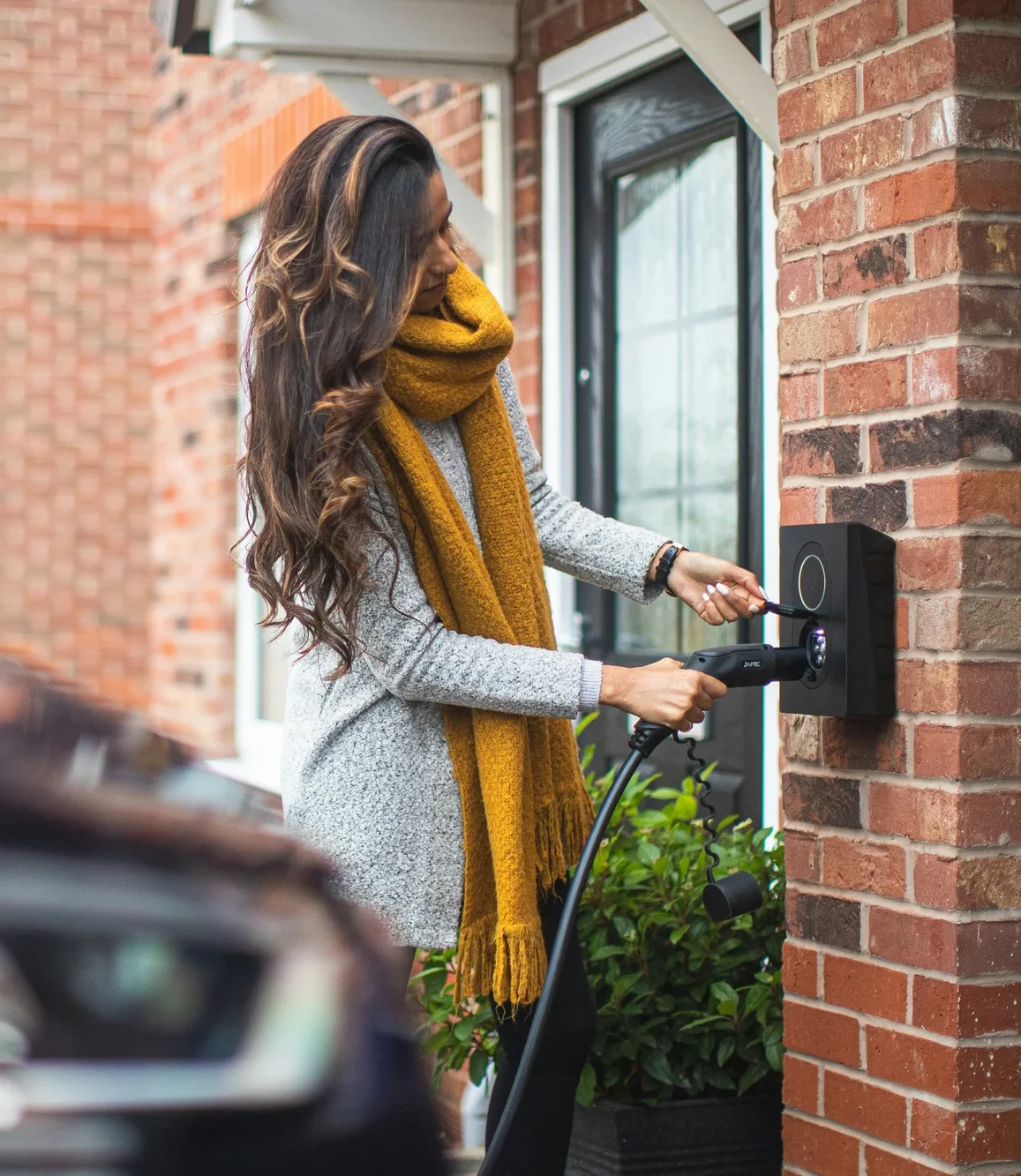 Woman plugging in her electric car outside a brick house.
