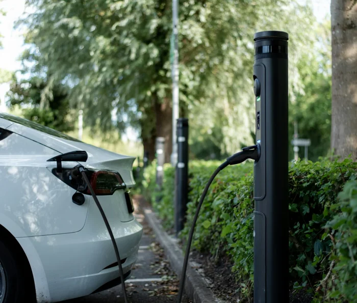 Electric car charging beside trees.